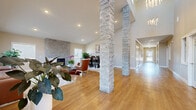 Located at Eden Garden Drive in Loveland, Colorado, this single-floor clubhouse offers a well-appointed, open-concept gathering space designed with both comfort and style in mind. The interior immediately impresses with soaring ceilings and dramatic stacked stone columns that serve as architectural focal points, anchoring the layout while adding a refined, natural texture to the space.

Warm hardwood flooring runs throughout, tying together the living and dining areas in a cohesive, inviting flow. The living area features a striking stone accent wall with a built-in fireplace flanked by windows that allow ample natural light to fill the room. Seating is arranged to encourage conversation, with a mix of leather and upholstered chairs complemented by layered area rugs.

The dining area offers a high-top table with substantial seating, positioned near windows that bring in additional daylight. Tasteful artwork, including a bold equine-themed piece, adds a locally inspired character to the dining space.

Near the entry, a double-height foyer showcases elegant pendant chandeliers suspended from the upper reaches of the ceiling, creating a grand first impression. The hallway connects seamlessly to the main gathering area, completing a layout that is both functional and visually engaging throughout.