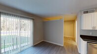 Located at 1107 Garner Rd in Raleigh, NC, this single-floor unit offers a well-designed layout with contemporary finishes throughout. The living area is bright and open, featuring wood-look flooring, neutral-toned walls, and sliding glass doors fitted with vertical blinds that allow an abundance of natural light while providing views of the surrounding greenery outside.

The kitchen is a standout feature, outfitted with crisp white shaker-style cabinetry, dark granite countertops, and a full suite of stainless steel appliances including a refrigerator, range, microwave, and dishwasher. Light wood-look flooring continues seamlessly from the living area into the kitchen, reinforcing a cohesive, modern aesthetic.

Additional rooms offer versatile living spaces with the same consistent wood-look flooring and neutral wall colors, each illuminated by ceiling-mounted light fixtures. Clean white baseboards and trim add a polished finishing touch throughout.

The bathroom features a full tub and shower combination, enclosed by classic white square tile, complemented by chrome fixtures and a towel bar, delivering a clean and functional design. Overall, the space presents a move-in-ready environment with modern updates and a bright, welcoming atmosphere ideal for comfortable everyday living.
