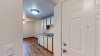 This single-floor residence offers a practical and comfortable layout with a variety of functional spaces throughout. The galley-style kitchen is well-appointed with white cabinetry accented by wood-toned upper cabinet trim, a dishwasher, a white electric range, a refrigerator, and a stainless single-basin sink with laminate countertops. Durable wood-look flooring runs through the kitchen and connects seamlessly to an adjacent dining or flex area, creating a cohesive flow. A dedicated laundry room, accessible from the kitchen, houses a full-size washer and dryer, adding significant everyday convenience. The living room is a standout space, featuring a brick-surround fireplace as its focal point, plush carpeting, and a large vertical-blind window that lets in generous natural light. A ceiling fan overhead adds to the room's comfort. The bedrooms are carpeted and bright, each benefiting from windows with vertical blinds that frame views of surrounding greenery. One bedroom includes a spacious sliding-door closet, offering ample storage. The textured ceilings appear throughout the home, adding subtle visual character. Overall, the space presents a clean, move-in-ready environment with a warm, understated aesthetic.