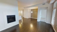 This single-floor residence offers a thoughtfully designed open-concept layout that seamlessly connects the living, dining, and kitchen areas. Rich, dark hardwood flooring runs throughout the main living space, providing warmth and a sense of continuity across the floor plan.

The living area is anchored by a sleek, modern fireplace set within a clean white surround, creating an inviting focal point. The open layout flows effortlessly into a dining area distinguished by an accent wall in a warm taupe tone and an elegant pendant light fixture that adds a refined touch overhead.

The kitchen is positioned at the rear of the main living space and features white cabinetry, a light-toned countertop, and stylish pendant lighting, offering both functionality and visual appeal. Recessed lighting throughout the ceiling ensures the space is well-lit and bright.

Architectural details such as structural beams and wide doorways add definition to each zone without disrupting the open flow of the layout. An adjacent room with lighter flooring visible through a wide corridor suggests additional flexible living or bedroom space. The overall ambiance is modern and clean, with a neutral color palette that provides an ideal backdrop for a variety of interior styles.
