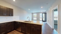 Located at 114 E Fifth Ave in Columbus, Ohio, this single-floor unit offers a thoughtfully designed open-concept layout that seamlessly connects the kitchen, dining, and living areas. The kitchen is a standout feature, equipped with dark espresso shaker-style cabinetry, light quartz countertops, a white subway tile backsplash, and a full suite of stainless steel appliances including a refrigerator, electric range, microwave, and dishwasher. A large peninsula with an integrated sink provides additional prep space and serves as a natural divider between the kitchen and the open living area. Warm wood-look plank flooring runs throughout the main living spaces, adding a cohesive and inviting aesthetic. The living area is bright and airy, featuring large windows and a glass-panel door that fill the space with natural light. The bedroom offers plush carpeting and corner windows that provide generous natural light. The bathroom is finished with wood-look tile flooring, dark cabinetry with a white countertop vanity, and a frameless sliding glass shower enclosure accented by marble-look tile surround. Recessed lighting throughout the unit enhances the clean, modern ambiance of this well-appointed Columbus residence.