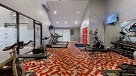 This 510 square foot fitness center in Denver, CO, is a well-equipped, single-floor space designed to cater to various workout needs. The room features a striking vaulted ceiling with recessed lighting and a large ceiling fan, creating an open and airy atmosphere. The most eye-catching element is the vibrant red and white geometric patterned carpet that covers the entire floor, adding energy and visual interest to the space.

The gym is outfitted with a comprehensive selection of exercise equipment. For cardio, there are multiple treadmills, elliptical machines, and stationary bikes. Strength training options include a full rack of free weights, weight benches, and various resistance machines. Exercise balls of different sizes and a dedicated area for floor exercises complete the offerings.

The space is further enhanced by wall-mounted TVs for entertainment during workouts, and large windows with white blinds that allow for natural light and temperature control. A set of bright red lockers provides storage for personal items. Mirrors line one wall, helping users maintain proper form during exercises.

The layout is thoughtfully arranged to maximize the available space, with clear zones for different types of workouts. This well-designed fitness center offers a complete gym experience within a compact area, making efficient use of its 510 square feet.