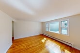 Located at 2 Lincoln St in Milford, Massachusetts, this two-bedroom, one-bathroom residence offers a practical and well-appointed single-floor layout. Warm hardwood flooring runs throughout the main living areas and bedrooms, lending a clean, consistent look to the space. The living room is bright and open, with large windows that invite natural light and views of the surrounding neighborhood. Baseboard heating is present throughout, ensuring year-round comfort. The combined dining and kitchen area is a functional highlight, featuring white shaker-style cabinetry, granite countertops, a stainless steel sink, and white appliances including an electric range and refrigerator. Light tile flooring and a window overlooking greenery complete the kitchen's airy feel. Both bedrooms are well-proportioned with hardwood floors, multiple windows providing cross-ventilation and natural light, and easy access to the five available closets distributed throughout the unit. The full bathroom includes a tiled tub/shower surround, a vanity with mirror, and a window for natural light and ventilation. Two entry points and a connecting hallway add to the unit's convenient flow. Overall, the space presents a tidy, move-in ready environment with classic finishes.