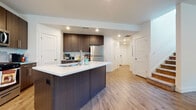 This two-story space showcases a clean, modern design aesthetic carried consistently throughout its layout. The kitchen serves as a central highlight, featuring rich dark wood-tone cabinetry with sleek hardware, crisp white quartz countertops, and a full suite of stainless steel appliances including a gas range, over-the-range microwave, and refrigerator. A generously sized kitchen island with an integrated sink provides additional workspace and casual seating. Light wood-style flooring flows seamlessly through the kitchen and into the adjacent dining area, where a window fitted with horizontal blinds allows natural light to brighten the space.

The main level also includes a convenient half bathroom, finished with matching dark wood-tone vanity cabinetry and wood-look flooring. A full bathroom on another level features a combined tub and shower with a curtain enclosure, complemented by the same cohesive cabinetry style.

The bedroom is a well-proportioned retreat finished with plush carpeting and equipped with a ceiling fan. Multiple windows, including elevated transom-style windows, allow natural light to filter in from several angles, creating an airy and comfortable atmosphere throughout the space.