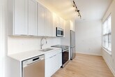 Located at 1100 Dahlia St NW in Washington, DC, this thoughtfully designed one-bedroom, one-bathroom unit offers a clean, modern aesthetic throughout. Light-toned hardwood flooring flows seamlessly across the entire space, creating a bright and cohesive feel.

The open-concept living and dining area is bathed in natural light from multiple large windows fitted with blinds, offering views of the surrounding neighborhood. The space transitions effortlessly into a well-appointed kitchen featuring crisp white shaker-style cabinetry extending to the ceiling, quartz countertops, a stainless steel sink, and a full suite of stainless steel appliances including a dishwasher, range, microwave, and refrigerator. Track lighting overhead adds a contemporary touch.

The bedroom is a comfortable, well-proportioned retreat with a window that draws in natural light. Two closets provide generous storage, one of which features wire shelving for added organization. A dedicated hallway connects the living areas to the private spaces, which include an in-unit laundry area for added convenience.

The bathroom is finished in a clean, neutral palette with a white vanity, tiled tub-shower combination with a curved curtain rod, and light wood-style flooring. The overall ambiance of the unit is modern, airy, and move-in ready.