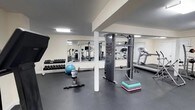 The Westgate fitness center is a dedicated, single-floor exercise facility designed to support a comprehensive workout experience. The gym features durable black rubber flooring throughout, providing both safety and functionality for a wide range of activities. A large wall-mounted mirror spans one side of the room, visually expanding the space and allowing users to monitor their form during exercise. The facility is equipped with a cable machine tower, ideal for a variety of strength training exercises, alongside a dumbbell rack stocked with a full range of free weights. A treadmill offers cardio training options, while additional equipment including a rowing machine, stationary bike, and step platforms round out the selection. A stability ball and other accessories are also available for functional fitness and flexibility work. The space is well-lit with overhead flush lighting and features clean white walls that contribute to a bright, motivating atmosphere. The layout is thoughtfully organized to allow comfortable movement between equipment stations. Whether focusing on strength, cardio, or cross-training, this fitness center provides residents and users with a practical and fully equipped environment to meet their fitness goals.