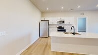 The 2B floorplan in Sterling Heights, Michigan is a thoughtfully designed single-floor residence offering two bedrooms, three bathrooms, and a dedicated closet. Light hardwood flooring flows consistently throughout the entire space, creating a cohesive and clean aesthetic.

The kitchen serves as a central highlight, featuring crisp white shaker cabinetry, white quartz countertops, and a full suite of stainless steel appliances including a refrigerator, electric range, built-in microwave, and dishwasher. A kitchen island with an undermount sink and matte black faucet provides additional workspace and a natural gathering point.

Both bedrooms are well-proportioned and receive ample natural light through large windows dressed with horizontal blinds. The primary bedroom offers a comfortable footprint with direct access to adjacent spaces. Each bedroom benefits from neutral wall tones that complement the light flooring.

The three bathrooms maintain a consistent modern design language, each featuring white vanity cabinetry with matte black hardware, white countertops, framed mirrors, and contemporary vanity lighting. A dedicated utility area houses a stacked washer and dryer alongside a water heater, maximizing functional use of space. Overall, the 2B floorplan presents a clean, modern, and move-in ready environment.
