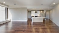 This sleek, single-floor residence showcases a thoughtfully designed open-concept layout, where rich, dark hardwood flooring flows seamlessly throughout every room, creating a sense of warmth and continuity. The open living area is expansive and bright, anchored by large floor-to-ceiling windows that frame sweeping panoramic city views and flood the interior with abundant natural light. Ceiling fans provide added comfort in the living and bedroom spaces.

The modern kitchen is a standout feature, equipped with stainless steel appliances including a full-size refrigerator and range, crisp white cabinetry paired with warm wood-toned upper cabinets, a subway tile backsplash, a sleek wall-mounted range hood, and a generous center island with a light wood finish and white quartz countertop. Pendant lighting above the island adds a stylish finishing touch, while recessed lighting ensures the space is well-illuminated throughout.

The bedroom is generously proportioned and benefits from a large picture window offering the same impressive cityscape views. The bathroom is outfitted with a double-sink vanity featuring a dark stone countertop, warm wood cabinetry, modern brushed-metal fixtures, and LED-backlit mirrors, delivering a refined and spa-like aesthetic. Overall, the space exudes a clean, contemporary character with high-quality finishes at every turn.