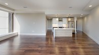 This sleek, single-floor residence showcases a thoughtfully designed open-concept layout, where rich, dark hardwood flooring flows seamlessly throughout every room, creating a sense of warmth and continuity. The open living area is expansive and bright, anchored by large floor-to-ceiling windows that frame sweeping panoramic city views and flood the interior with abundant natural light. Ceiling fans provide added comfort in the living and bedroom spaces.

The modern kitchen is a standout feature, equipped with stainless steel appliances including a full-size refrigerator and range, crisp white cabinetry paired with warm wood-toned upper cabinets, a subway tile backsplash, a sleek wall-mounted range hood, and a generous center island with a light wood finish and white quartz countertop. Pendant lighting above the island adds a stylish finishing touch, while recessed lighting ensures the space is well-illuminated throughout.

The bedroom is generously proportioned and benefits from a large picture window offering the same impressive cityscape views. The bathroom is outfitted with a double-sink vanity featuring a dark stone countertop, warm wood cabinetry, modern brushed-metal fixtures, and LED-backlit mirrors, delivering a refined and spa-like aesthetic. Overall, the space exudes a clean, contemporary character with high-quality finishes at every turn.