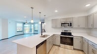 This well-appointed 3-bedroom, 2-bathroom apartment in Jeffersonville, Indiana offers a thoughtfully designed single-floor layout with modern finishes throughout. The open-concept kitchen serves as the heart of the home, featuring gray shaker-style cabinetry, white quartz countertops, a large center island with a pendant-lit overhang and undermount sink, and a full suite of stainless steel appliances including a refrigerator, electric range, microwave, and dishwasher. Light hardwood-style flooring flows through the kitchen and living areas, creating a seamless, cohesive feel. The bright living room benefits from abundant natural light through multiple windows and sliding glass doors that open to a private balcony with open outdoor views. Each bedroom is carpeted and equipped with a ceiling fan, and the spacious primary bedroom includes its own walk-in closet with wire shelving. A total of four closets provide ample storage throughout the unit. The two bathrooms are finished with gray vanity cabinetry, white quartz counters, and light wood-style flooring. A dedicated in-unit laundry room houses a full-size washer and dryer alongside the home's mechanical systems. Clean white walls and dark door and window trim accents lend a crisp, contemporary aesthetic throughout.