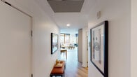 This thoughtfully designed single-floor residence combines modern aesthetics with functional living across a well-appointed layout. An inviting entryway corridor, adorned with curated artwork, leads into the heart of the home. The open-concept kitchen is a standout feature, outfitted with light wood cabinetry, subway tile backsplash, dark stone countertops, and a full suite of stainless steel appliances including a gas range and built-in microwave. A peninsula with seating for two, illuminated by globe pendant lights on a brass track, seamlessly connects the kitchen to the living and dining areas. The living room is anchored by expansive floor-to-ceiling windows framed in warm wood, offering views of the surrounding urban streetscape and flooding the space with natural light. Light hardwood flooring flows throughout, enhancing the airy, cohesive feel. The bedroom is a tranquil retreat, featuring oversized windows with leafy tree views, a sliding barn door entry, and a spa-like en-suite bathroom with warm tile flooring, a floating wood vanity, and a glass-enclosed walk-in shower. A full bathroom with in-unit stacked washer and dryer provides added convenience. Throughout the residence, clean white walls and refined finishes create a bright, contemporary ambiance.