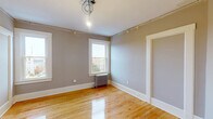 Located at 85–97 S Pleasant St in Amherst, MA, this single-floor unit offers four bedrooms, two bathrooms, a kitchen, pantry, and closet across a well-organized layout. Warm hardwood floors run throughout, lending a cohesive and classic character to every room. The neutral gray walls provide a clean, versatile backdrop across all four bedrooms, each featuring white-trimmed windows that invite natural light and views of the surrounding neighborhood. Cast-iron radiators in several rooms speak to the building's historic charm while providing efficient heating. The kitchen stands out with bold navy-blue shaker cabinets, granite-look countertops with an undermount sink, subway tile backsplash, and stainless steel appliances including a range and French door refrigerator. An adjoining pantry with coat hooks adds practical storage. Two hallways connect the rooms efficiently throughout the unit. The primary bathroom is elegantly appointed with black-and-white mosaic tile flooring, a dark vanity with marble countertop, gold hardware, a subway-tiled shower, and a framed mirror. The second bathroom offers a more compact design with wood-tone cabinetry and matte black fixtures. The spacious primary bedroom provides generous room for furnishings and features dual windows with neighborhood views.