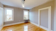Located at 85–97 S Pleasant St in Amherst, MA, this single-floor unit offers four bedrooms, two bathrooms, a kitchen, pantry, and closet across a well-organized layout. Warm hardwood floors run throughout, lending a cohesive and classic character to every room. The neutral gray walls provide a clean, versatile backdrop across all four bedrooms, each featuring white-trimmed windows that invite natural light and views of the surrounding neighborhood. Cast-iron radiators in several rooms speak to the building's historic charm while providing efficient heating. The kitchen stands out with bold navy-blue shaker cabinets, granite-look countertops with an undermount sink, subway tile backsplash, and stainless steel appliances including a range and French door refrigerator. An adjoining pantry with coat hooks adds practical storage. Two hallways connect the rooms efficiently throughout the unit. The primary bathroom is elegantly appointed with black-and-white mosaic tile flooring, a dark vanity with marble countertop, gold hardware, a subway-tiled shower, and a framed mirror. The second bathroom offers a more compact design with wood-tone cabinetry and matte black fixtures. The spacious primary bedroom provides generous room for furnishings and features dual windows with neighborhood views.
