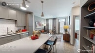 Located at 905 W Main St in the heart of Durham, NC, this one-bedroom, one-bathroom residence offers a thoughtfully designed open-concept layout finished with light wood-style flooring throughout. The kitchen serves as a central hub, showcasing sleek gray flat-front cabinetry, a classic white subway tile backsplash, stainless steel appliances, and a spacious white quartz island with seating for two — illuminated by industrial-style pendant lights. The kitchen flows seamlessly into the living room, where large windows with plantation shutters allow abundant natural light and provide a welcoming ambiance. The bedroom features a striking navy accent wall, ceiling fan, and generous windows that continue the theme of natural light. A dedicated closet with built-in shelving and hanging storage connects directly to the bathroom, which includes a tiled walk-in shower and wood-style flooring. Additional conveniences include a utility room and in-unit laundry. The space is efficiently organized across a single floor, making it ideal for comfortable urban living in one of Durham's most vibrant neighborhoods.