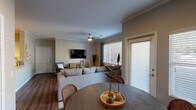 Located at 7520 S Utica Dr in Littleton, Colorado, this single-floor residence offers a thoughtfully designed layout with a cohesive, modern aesthetic. Rich hardwood-style flooring runs throughout the space, creating a warm and unified foundation.

The open-concept living and dining area is anchored by a ceiling fan, crown molding, and large windows dressed with blinds and drapes that allow ample natural light to fill the room. A wall-mounted flat-screen TV, generous sectional seating, and direct access to an exterior door make the living space both functional and inviting.

The dining area features a bold, dark accent wall adorned with a large abstract artwork, complemented by a round table and built-in white shelving — adding both character and practical storage.

The kitchen is well-equipped with stainless steel appliances including a refrigerator, range, and microwave, set against crisp white cabinetry and light countertops. A peninsula with a sink provides additional prep space and informal seating potential. A nearby built-in shelving unit adds extra storage convenience.

The bedroom is a comfortable retreat with a sliding glass door opening to an outdoor area, a dedicated walk-in closet with built-in shelving, and a dark accent wall that adds a sophisticated touch.

The bathroom includes a full tub-shower combination with classic white tile surround and a vanity with ample counter space.