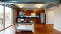 Located at 3144 S Chowen Ave in Minneapolis, MN, this single-floor urban unit blends modern finishes with industrial-inspired design elements. The open-concept layout is anchored by rich hardwood flooring that flows seamlessly throughout the main living areas, complemented by exposed metal ductwork along the ceiling that adds a distinctive loft-like character.

The kitchen is a standout feature, showcasing warm wood cabinetry, dark granite countertops, and a full suite of stainless steel appliances including a range, over-the-range microwave, dishwasher, and refrigerator. Flush ceiling light fixtures illuminate the space, while a large window at the far end of the living area allows generous natural light to fill the room and provides views of the surrounding neighborhood.

The entry hallway is well-organized, flanked by multiple doors offering access to additional rooms and storage. The bathroom is finished with large-format stone tile flooring, a dark wood vanity with a white countertop, a tub-shower combination with tile surround, and bright vanity lighting above the mirror. The overall ambiance is clean, contemporary, and functional — suited for urban living in the heart of Minneapolis.