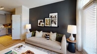 Located at 1000 Fazio Dr in Southern Pines, NC, this single-floor residence offers a carefully curated interior defined by bold design choices and quality finishes. The living area makes an immediate impression with a dramatic charcoal accent wall serving as a backdrop for a tufted sofa, layered throw pillows, and a wall-mounted art ledge displaying a curated gallery arrangement. Ambient table lamps on each side complete the polished, contemporary look.

The kitchen is outfitted with soft gray shaker-style cabinetry, frosted upper glass-front cabinets, light marble-look countertops, a classic white subway tile backsplash, and stainless steel appliances — combining both style and functionality in a compact, efficient layout. Light hardwood-style flooring runs throughout the main areas, adding warmth and continuity.

The bedroom is a standout space, wrapped in a rich forest green accent wall adorned with a decorative arrangement of vintage golf club art — a nod to the area's renowned golf heritage. A ceiling fan, soft carpeting, and generous natural light from large windows create a comfortable and inviting retreat.

The bathroom features gray cabinetry with brushed gold hardware, a marble-look countertop, hardwood-style flooring, and a tub-shower combination — clean, modern, and well-appointed. Overall, this residence blends contemporary design with locally inspired touches for a distinctive living experience.