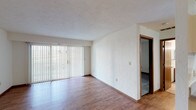 This single-floor unit in Columbia, Illinois offers a functional and straightforward layout designed for comfortable everyday living. The main living area is spacious and open, featuring warm hardwood-style flooring and neutral white walls that create a bright, clean atmosphere. A large sliding glass door fitted with vertical blinds anchors one end of the living space, allowing natural light to filter in while providing access to an outdoor area. The textured ceiling adds subtle character throughout the main living zones.

The kitchen is positioned adjacent to the living area in a pass-through configuration, featuring a raised counter that separates the two spaces. It includes a coil-burner electric range, a sink, and wood-toned cabinetry, offering practical functionality. A pendant light fixture illuminates the entry area nearby, where a front door and a large closet provide storage and a clear point of arrival.

The bedroom is carpeted for added comfort and includes a window with vertical blinds that brings in natural light. A closet is accessible directly from the bedroom. The bathroom features tile flooring, a combined tub and shower unit, a vanity with a wall-mounted mirror, and warm wood-toned cabinetry, completing this practical and well-organized living space.