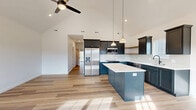 Located at 5709 Trailside W Cir in Springfield, MO, this single-story, 2-bedroom, 2-bathroom home offers a thoughtfully designed layout with modern finishes throughout. The heart of the home is a striking open-concept kitchen and living area defined by dramatic vaulted ceilings that create an impressive sense of height and volume. The kitchen is outfitted with slate-blue shaker-style cabinetry, crisp white quartz countertops, a subway tile backsplash, stainless steel appliances including a built-in microwave and French door refrigerator, a center island, and warm wood open shelving. Pendant lighting and recessed fixtures add character and functionality. Light wood-tone flooring runs seamlessly throughout the main living areas, complementing the bright, neutral palette. The living room features a vaulted ceiling with a ceiling fan and a front entry door flanked by windows that draw in abundant natural light. The bedrooms are comfortably sized with ceiling fans and large windows, while the bathrooms include a full soaking tub with surround. Additional highlights include two closets, a dedicated laundry area, and a spacious attached garage with a concrete floor and automatic door opener. This home delivers a clean, contemporary aesthetic with practical, well-organized living spaces.