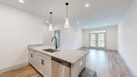 This well-designed one-bedroom, one-bathroom unit offers a thoughtfully organized single-floor layout with modern finishes throughout. The open-concept kitchen serves as the centerpiece of the main living area, featuring a granite-topped peninsula island with an undermount sink and matte black faucet, white shaker-style cabinetry, a subway tile backsplash, and a full suite of stainless steel appliances. Stylish pendant lights hang above the island, complementing the recessed lighting overhead. Wood-look flooring extends throughout the kitchen and living area, adding warmth and cohesion to the space.

The living room is bright and airy, anchored by French doors with transom windows that open to a private balcony and bring in abundant natural light. The bedroom offers plush carpeting, a ceiling fan, and a large window with outdoor views. The bathroom is finished with a granite-topped vanity, wood-look flooring, a soaking tub, and matte black hardware accents. A dedicated closet with wire shelving provides practical storage. The unit's clean, neutral palette and consistent modern design elements create a cohesive and comfortable living environment throughout.