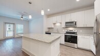 This well-appointed single-floor unit offers a clean, modern aesthetic throughout, combining functional design with quality finishes. The heart of the home is a thoughtfully designed kitchen that impresses with crisp white cabinetry, light granite countertops, and a full suite of stainless steel appliances, including a range, microwave, refrigerator, and dishwasher. A subway tile backsplash adds a classic touch, while a central island with matching granite provides additional workspace and casual seating. Pendant lighting and recessed fixtures illuminate the space, and light wood-tone flooring ties the kitchen and adjacent living areas together seamlessly. The bedrooms feature neutral carpet and bright windows with blinds, allowing natural light to filter in while maintaining privacy. Each room is finished with clean white walls and ceiling fans, contributing to a calm, airy atmosphere. The bathroom is outfitted with wood-look flooring, a tub-shower combination with tiled surround, and brushed nickel grab bars and fixtures for a polished, practical finish. A dedicated laundry room houses a full-size Whirlpool washer and dryer alongside overhead shelving, offering convenient in-unit functionality. Overall, the space presents a cohesive, contemporary living environment designed for comfort and ease.