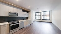 Located in the heart of Chicago's Loop at 29 S LaSalle Street, this modern studio offers a thoughtfully designed single-floor layout with a clean, contemporary aesthetic throughout. The open-concept kitchen and living area serves as the centerpiece of the unit, featuring a sleek, wall-length kitchen outfitted with stainless steel appliances — including a gas range, microwave, dishwasher, and refrigerator — complemented by two-tone cabinetry in white and natural wood, a dark herringbone tile backsplash, and light quartz countertops. Hardwood-style flooring flows seamlessly throughout the space, adding warmth and continuity. The living area is bathed in natural light through large, black-framed windows that frame views of the surrounding downtown Chicago architecture. A dedicated closet with bifold doors provides ample built-in storage. The bathroom is finished with white subway tile in the walk-in shower, a floating wood-toned vanity, a mirrored medicine cabinet, and matte black fixtures, conveying a refined, modern sensibility. An in-unit laundry area and a clean, minimalist hallway round out this efficiently designed space. Recessed lighting throughout ensures a bright and inviting atmosphere.