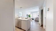 Located at 1650 Ferry Wharf Road in Kelowna, BC, this well-appointed 2-bedroom, 2-bathroom unit offers a thoughtfully designed layout across a single floor. The open-concept kitchen and living area serves as the heart of the home, featuring light wood-look flooring, white flat-panel cabinetry, stainless steel appliances, and a generous island with bar seating — ideal for both everyday living and entertaining. The living room is bright and welcoming, with large windows that allow natural light to fill the space and provide outdoor views.

Both bedrooms are comfortably sized, with the primary bedroom offering a dedicated closet and natural light from a large window with exterior views. The second bedroom is equally well-lit and includes its own closet. Each room features a clean, minimalist aesthetic consistent with the overall design.

The two bathrooms are distinctly finished: one includes a full soaker tub with a curtained surround and a single vanity with tile flooring, while the ensuite bathroom offers a glass-enclosed walk-in shower, a wide grey vanity with white quartz countertop, large-format tile flooring, and a backlit mirror. The unit also includes in-suite laundry. Clean lines, neutral tones, and modern fixtures define this contemporary Kelowna residence.
