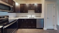 This single-floor 2-bedroom, 2-bathroom residence offers a clean, modern aesthetic throughout its thoughtfully designed layout. The open living area is anchored by rich, dark hardwood-style flooring and filled with natural light through large French doors that open to an outdoor view, creating an inviting and airy atmosphere.

The kitchen is a functional highlight, featuring dark espresso cabinetry with sleek hardware, light marble-toned countertops, a stainless steel undermount sink, and a full suite of stainless steel appliances including a refrigerator, range, built-in microwave, and dishwasher. A hallway connects the living and kitchen areas seamlessly, maintaining an efficient flow throughout the unit.

Both bedrooms are carpeted in a neutral, soft-toned carpet and offer bright windows that allow ample natural light. Each room provides a calm, versatile space with closet access and clean white walls.

The two bathrooms are finished with large-format tile flooring and dark espresso vanity cabinetry topped with light stone-style countertops. One bathroom features a full tub-shower combination, while the other offers a spacious vanity with a wide mirror and modern light fixtures, both designed with a consistent and polished style throughout.