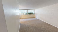 Located at 2040 Wheaton Way in Bremerton, WA, this 2-bedroom, 1-bathroom unit offers a practical and comfortable single-floor layout. The combined kitchen and living room area forms the heart of the unit, where the living space features wall-to-wall carpeting, a textured ceiling, and wide windows that invite natural light and outdoor views of surrounding greenery. A distinctive exposed wood beam adds architectural character to the living area, which also includes a built-in wall heater. The kitchen is efficiently laid out with warm honey-toned cabinetry, dark granite-style countertops, tile flooring, and white appliances including a refrigerator, electric range, and microwave. Both bedrooms are carpeted and feature large windows with vertical blinds, providing ample natural light. The primary bedroom offers generous closet space with dual sliding-door closets. Painted concrete block walls appear throughout the unit, lending a sturdy, solid construction character. The bathroom is finished with tile flooring, a wood-toned vanity with stone-style countertop, and a full tub-shower combination. Hallways connect the rooms efficiently within the thoughtfully organized floor plan.