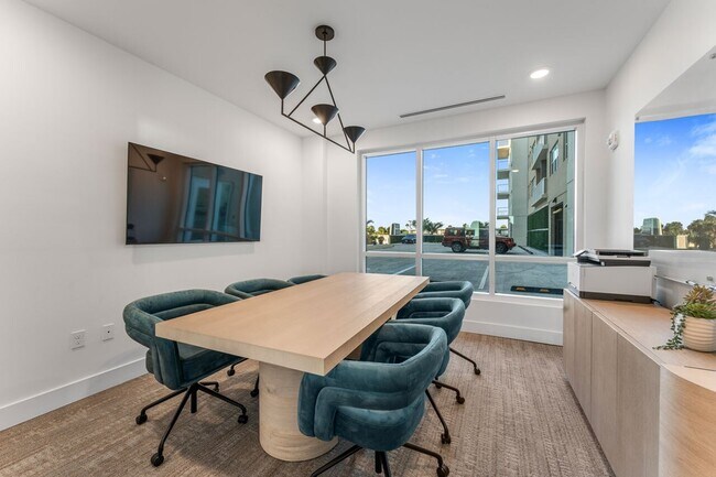 Moderna sala de conferencias con una elegante mesa de madera, seis lujosas sillas color verde azulado y una gran ventana que ofrece un ambiente luminoso y espacioso. - Triton Cay - Daytona Apartments