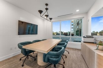Modern conference room with a sleek wooden table, six plush teal chairs, and a large window offering a bright, spacious atmosphere. - Triton Cay - Daytona Apartments