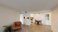 This single-floor model unit at 444 4th Avenue in Escondido offers a well-organized and functional layout designed for comfortable everyday living. The open living area flows seamlessly into the dining space, both finished with light wood-style flooring that extends throughout most of the unit. A half-wall partition separates the living and dining areas from the kitchen, which features a practical galley configuration with white shaker-style cabinetry, granite-look countertops, a decorative tile backsplash, and black appliances including a refrigerator and electric range. A ceiling fan overhead keeps the dining area comfortable. The living room benefits from natural light and provides access to an outdoor balcony or patio through a sliding glass door framed by vertical blinds. The unit includes two well-proportioned bedrooms, each with wood-style flooring and windows that invite natural light and outdoor greenery views. Two bathrooms serve the unit — one features a shower-tub combination with a wide vanity mirror and stone-look countertop, while the second offers a streamlined layout with matching finishes. Textured ceilings are present throughout, and the overall palette of neutral whites and warm tones creates a clean, inviting ambiance throughout the space.