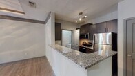Located in the Country Walk community in Snellville, Georgia, this single-story 1-bedroom, 1-bathroom residence offers a thoughtfully designed layout with modern finishes throughout. The living area serves as the centerpiece of the home, showcasing a distinctive tray ceiling with crown molding detail and a ceiling fan, creating an elevated sense of space. Wood-style flooring flows through the main living areas, adding warmth and cohesion, while French doors invite natural light and provide access to the outdoors.

The kitchen is designed for both function and style, featuring granite countertops, dark cabinetry, and a full suite of stainless steel appliances including a refrigerator, range, and microwave. A peninsula counter with an undermount sink opens toward the living area, creating a convenient and connected layout. Track lighting illuminates the kitchen workspace effectively.

The bedroom is a comfortable retreat with plush carpeting, a sizable window overlooking greenery, and a textured ceiling. The bathroom is clean and modern, equipped with a granite-topped vanity, dark cabinetry with brushed nickel hardware, a large mirror, and light wood-style flooring. The overall ambiance of the unit is contemporary and move-in ready, reflecting a practical yet polished living environment.
