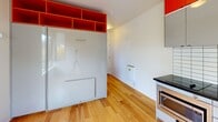 Located in Seattle's Roosevelt neighborhood, this efficiently designed studio unit at 838 NE 69th St, Unit 310, makes excellent use of its compact footprint. The main living area features warm-toned light hardwood flooring throughout, crisp white walls, and a large corner window fitted with a roller shade that invites natural light and offers treetop views of the surrounding greenery.

The kitchen is a standout feature, boasting bold design choices including high-gloss gray cabinetry, vibrant orange upper shelving, a white subway tile backsplash, dark countertops, and stainless steel appliances — including a refrigerator, range, and built-in microwave. The layout is highly functional despite its compact scale.

A built-in Murphy bed system with integrated open orange shelving above maximizes the versatility of the living space, allowing the room to serve multiple purposes throughout the day.

The bathroom is sleekly finished with large-format dark floor tiles, floor-to-ceiling white wall tiles, a walk-in shower, a wall-mounted sink, and a small frosted window for natural ventilation. The overall aesthetic of the unit is clean, modern, and purposefully designed, making it a well-appointed space for efficient urban living in Seattle.
