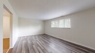 Located at 80 W Mill St in Springboro, Ohio, this single-floor residence offers three bedrooms, one bathroom, a kitchen, and a closet within a well-organized layout. Consistent grey-toned luxury vinyl plank flooring runs throughout the entire unit, providing a clean, cohesive aesthetic from room to room.

The spacious primary bedroom is notably generous in size, featuring a large sliding-door closet and access to the full bathroom, which is equipped with a tub-shower combination, a single vanity with wood cabinetry, and a wall mirror. The two additional bedrooms are bright and comfortable, each featuring windows that allow natural light and views of the surrounding greenery.

The galley-style kitchen is efficiently designed with dark wood cabinetry lining both walls, white countertops, a double sink, and white appliances including an electric range and refrigerator. An overhead range hood and ceiling light fixture complete the functional cooking space.

Throughout the unit, neutral cream-toned walls complement the flooring, creating a bright and airy atmosphere. The floor plan, as shown in the dollhouse view, reflects a straightforward and practical layout that maximizes the use of available space. This unit offers a comfortable and move-in ready living environment in Springboro, OH.