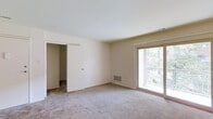 This single-floor residence offers a clean, functional layout designed for comfortable everyday living. The main living area is generously proportioned, featuring neutral wall-to-wall carpeting that adds warmth underfoot and a soft, understated aesthetic throughout. Crisp white ceilings and light-toned walls create a bright, open atmosphere that feels welcoming and versatile.

A standout feature of the main room is the large sliding glass door that opens to a private balcony enclosed by a classic brick railing. This door floods the interior with natural light and provides pleasant views of the surrounding greenery, creating a seamless connection between the indoor and outdoor spaces.

The room also includes a floor-mounted HVAC vent, ensuring efficient climate control year-round. A sliding door along one wall leads to an adjacent room or closet space, adding to the overall functionality and storage potential of the layout.

The space is presented in a neutral, move-in ready condition, offering a blank canvas that can easily be personalized to suit a variety of tastes and furnishing styles. The combination of natural light, outdoor access, and a straightforward, practical floor plan makes this a well-rounded residential space suitable for a range of living arrangements.