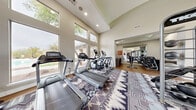 Located at 16356 N Thompson Peak Parkway in Scottsdale, Arizona, the KOTA Fitness Centre is a well-appointed, single-floor facility designed to support a comprehensive workout experience. The space features soaring ceilings with expansive floor-to-ceiling windows that flood the interior with natural light and offer views of the surrounding desert landscaping, creating an open and energizing atmosphere.

The main cardio area is outfitted with multiple treadmills, elliptical trainers, and a stationary bike, all positioned to take advantage of the natural light and outdoor views. A dedicated TKO functional training zone includes a multi-purpose power rack with TRX suspension straps, a hanging heavy punching bag, and a set of kettlebells — ideal for strength and conditioning workouts. An adjoining strength area houses a full rack of dumbbells, medicine balls, stability balls, and a spin bike, complemented by large wall mirrors that enhance the sense of space.

The flooring transitions between warm hardwood and a bold, patterned area rug that adds a distinctive Southwest-inspired aesthetic throughout. Recessed lighting and a skylight in the secondary area ensure consistent illumination. The facility is accessed through a glass-panel door and is clearly branded as the KOTA Fitness Centre, offering residents a dedicated and thoughtfully designed space for their fitness goals.