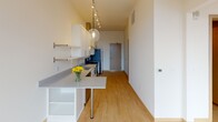 Located at 104 N First St in Minneapolis's vibrant North Loop neighborhood, this single-floor unit showcases a clean, contemporary design with light hardwood-style flooring and a bright, neutral palette throughout. The open kitchen is a standout feature, outfitted with crisp white shaker cabinetry, light quartz countertops, and a full suite of stainless steel appliances, including a range with a prominent steel hood vent, refrigerator, dishwasher, and built-in microwave. A peninsula with an extended countertop provides additional workspace and casual dining potential, while track lighting and a globe pendant fixture add modern character overhead. Floor-to-ceiling windows anchor the living area, flooding the space with natural light and offering elevated views of the surrounding Minneapolis skyline and cityscape. A ceiling fan complements the airy feel of the main living zone. In-unit laundry is conveniently accommodated with a stacked washer and dryer unit, accessible from a dedicated hallway. The bathroom features a white vanity with ample drawer storage, a large mirror, and tile flooring, maintaining the clean aesthetic found throughout the unit. Light wood-toned door frames and finishes add warmth to the otherwise modern interior.