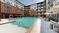 Located at 215 Reformation Pky in Canton, GA, this outdoor amenity space presents a thoughtfully designed resort-style pool courtyard that serves as a central gathering hub. The large, crystal-clear swimming pool is the undisputed focal point, reflecting the surrounding multi-story brick building with its blend of classic masonry and contemporary architectural detailing. The building's private balconies overlook the courtyard, creating an immersive, community-centered atmosphere.

The pool deck is generously appointed with cushioned lounge chairs paired with shade umbrellas, offering ample space for sunbathing and relaxation. A dedicated seating and dining area with patio furniture provides an inviting setting for outdoor gatherings. Toward the rear of the courtyard, additional amenities including an outdoor grill station and a cozy lounge area with plush seating are nestled alongside lush landscaping and mature trees that back up to a natural green backdrop.

The paver-finished deck surrounds the pool on all sides, offering a clean, polished aesthetic that complements the warm brick tones of the building. String lights are strung overhead in portions of the deck, adding a welcoming ambiance for evening use. The open-sky design ensures abundant natural light throughout the day, making this outdoor space a vibrant and functional retreat in the heart of Canton, Georgia.