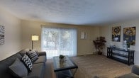 This 3-floor property offers a comfortable and functional layout across multiple levels. The living area is a welcoming space characterized by warm, neutral-toned walls and wall-to-wall carpeting that adds a sense of coziness underfoot. A prominent feature of the room is the large sliding glass door fitted with vertical blinds, which fills the space with natural light and provides views of the greenery outside, creating a pleasant indoor-outdoor connection.

The textured ceiling adds a classic architectural detail to the room, while the layout comfortably accommodates seating and a central coffee table, suggesting a well-proportioned gathering space. A floor lamp in the corner complements the natural light, and decorative touches such as framed wall art and a potted plant contribute to the overall warmth of the interior. The space appears clean and well-maintained, offering a straightforward and livable design that prioritizes comfort and practicality across its three floors.