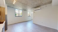Located at 1147 NW Eighth Ave in Miami, FL, this single-floor unit offers a thoughtfully designed layout comprising one bedroom and one bathroom. The interior showcases a contemporary aesthetic defined by exposed concrete ceilings that lend an industrial character, paired with crisp white walls and large-format neutral floor tiles throughout.

The main living area flows seamlessly into a well-appointed kitchen, which features a combination of white upper cabinetry and warm wood-toned lower cabinets, stainless steel appliances including a refrigerator, dishwasher, and built-in microwave, and clean countertops. A floor-to-ceiling window floods the kitchen and living area with abundant natural light, framing views of surrounding greenery.

The spacious bedroom is served by a wall-mounted split air conditioning unit and benefits from multiple windows that invite in natural light and outdoor views. The open, airy feel of the room is enhanced by the exposed concrete ceiling and neutral tile flooring.

The bathroom is a standout feature, showcasing marble-style porcelain tile surrounds in the tub-shower combination, with elegant grey veining against a white background. Chrome fixtures and a clean, minimalist design complete the space.

Overall, this unit presents a modern, urban aesthetic with industrial design elements and quality finishes throughout.