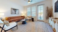 This furnished 920-square-foot apartment features two bedrooms and two bathrooms across a single floor, designed with a clean, contemporary aesthetic. Light wood-style flooring runs throughout the unit, creating a cohesive and bright atmosphere.

The open-concept kitchen and living area serves as the central hub of the unit. The kitchen is equipped with stainless steel appliances—including a refrigerator, range, microwave, and dishwasher—gray cabinetry, white countertops, a subway tile backsplash, and a peninsula with bar seating. A dedicated countertop bar area provides additional prep or serving space. The adjoining living room features large windows and a glass door that invite ample natural light and outdoor views, complemented by a ceiling fan.

The primary bedroom measures 160 square feet and includes dual windows with outdoor views. Both bedrooms offer light-filled interiors with neutral-toned walls. The primary bathroom features a double-sink vanity with gray cabinetry, a large mirror, and a shower-tub combination. The second bathroom mirrors a similar clean design with a single vanity and shower-tub combo.

A dedicated laundry room houses a full-size washer and dryer with overhead shelving for added storage.