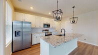 Located at 6480 Alexander Clay in Columbus, Ohio, this single-floor home combines modern design with functional living spaces. The kitchen serves as the centerpiece of the home, showcasing a large granite-topped island with an undermount sink, white shaker cabinetry with matte black hardware, a decorative arabesque tile backsplash, and a full suite of stainless steel appliances. A pair of geometric black lantern pendant lights hang above the island, adding an elegant focal point. Natural light flows in through multiple windows, brightening the hardwood-style flooring that runs throughout the main living areas. The bedrooms feature plush carpet and generously sized windows that invite additional natural light, creating warm, comfortable retreats. Select bedrooms include walk-in closets with built-in shelving for ample storage. The bathrooms are finished with granite vanity tops, white cabinetry, matte black fixtures, and large framed mirrors. A convenient half bath with hardwood-style flooring offers additional functionality. Neutral warm tones on the walls complement the clean white trim and doors throughout, creating a cohesive and inviting atmosphere. The open layout connects the kitchen and living areas seamlessly, making this home well-suited for both everyday living and entertaining.
