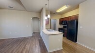This single-story, one-bedroom, one-bathroom residence offers a practical and cohesive layout designed for comfortable everyday living. The heart of the home is an open-concept space that seamlessly integrates the kitchen, dining, and living areas. The kitchen features rich, dark wood cabinetry, granite-style countertops, a peninsula island with a built-in sink, pendant lighting, and a full suite of black appliances including a refrigerator, range, and microwave. Wood-style plank flooring runs throughout the entire unit, lending a warm and consistent aesthetic. An arched entryway adds an architectural detail that connects the living area to the hallway.

The bedroom is a generously sized, private retreat with vaulted ceilings, multiple windows with blinds for natural light control, and access to a spacious walk-in closet outfitted with hanging rods and built-in shelving. An additional closet provides further storage flexibility.

The bathroom is well-equipped with a dark wood vanity, granite-style countertop, a large mirror, and accessibility grab bars. A dedicated laundry room with shelving, appliance hookups, and an electrical panel rounds out the unit's functional amenities. A pantry provides additional kitchen storage, and a glass-paneled entry door with a sidelight window welcomes natural light into the living area.