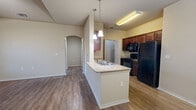 This single-story, one-bedroom, one-bathroom residence offers a practical and cohesive layout designed for comfortable everyday living. The heart of the home is an open-concept space that seamlessly integrates the kitchen, dining, and living areas. The kitchen features rich, dark wood cabinetry, granite-style countertops, a peninsula island with a built-in sink, pendant lighting, and a full suite of black appliances including a refrigerator, range, and microwave. Wood-style plank flooring runs throughout the entire unit, lending a warm and consistent aesthetic. An arched entryway adds an architectural detail that connects the living area to the hallway.

The bedroom is a generously sized, private retreat with vaulted ceilings, multiple windows with blinds for natural light control, and access to a spacious walk-in closet outfitted with hanging rods and built-in shelving. An additional closet provides further storage flexibility.

The bathroom is well-equipped with a dark wood vanity, granite-style countertop, a large mirror, and accessibility grab bars. A dedicated laundry room with shelving, appliance hookups, and an electrical panel rounds out the unit's functional amenities. A pantry provides additional kitchen storage, and a glass-paneled entry door with a sidelight window welcomes natural light into the living area.