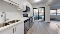 Located at 1791 King St in Hamilton, Ontario, this 2-bedroom, 1-bathroom unit offers a thoughtfully designed single-floor layout with a clean, modern aesthetic throughout. Light wood laminate flooring flows seamlessly across all rooms, complemented by crisp white walls, crown moulding, and white baseboards that add a polished finish.

The entrance leads into a well-organized layout connecting the main living areas. The kitchen is a standout feature, boasting white shaker-style cabinetry with brushed nickel hardware, a white subway tile backsplash, light quartz countertops, and stainless steel appliances including a fridge, stove, microwave, and dishwasher. A sliding glass door in the kitchen opens directly onto a private balcony with outdoor views.

The combined dining and kitchen area flows naturally into the living room, which offers generous proportions and large windows that bring in ample natural light. Both bedrooms are well-sized, with the primary bedroom offering a comfortable footprint, large windows with garden views, and access to closet storage. The second bedroom is equally bright with a large black-framed window.

The bathroom features a full soaker tub with a handheld showerhead, white subway tile surround, and a decorative mosaic tile accent border. Additional conveniences include in-unit laundry and multiple closets throughout.