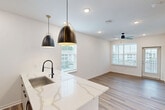 Located in Ponte Vedra Beach, FL, this well-designed one-bedroom, one-bathroom residence offers a thoughtful layout that maximizes comfort and functionality. The open-concept kitchen and living area serves as the heart of the home, showcasing a striking waterfall-edge quartz island with an integrated sink and matte black fixtures. Two pendant lights with gold accents hang above, complementing the two-tone cabinetry — crisp white lowers paired with warm wood-toned uppers — and a matching quartz backsplash. Stainless steel appliances, including a French door refrigerator, range, and built-in microwave, complete the modern kitchen. Durable wood-look flooring flows throughout the main living areas, adding warmth and visual continuity. The bedroom offers a comfortable and private retreat, featuring soft carpeting, a ceiling fan, and windows with horizontal blinds that allow natural light while maintaining privacy. A double-door closet provides generous storage. The bathroom is finished with wood-look tile flooring, a sleek vanity with wood-toned cabinetry, an illuminated mirror, and a full tub-shower combination enclosed by a glass door. Clean white walls and neutral tones throughout the space create a fresh, move-in-ready ambiance ideal for those seeking modern living in a coastal Florida community.