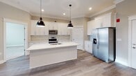 Located at 1154 Westyn Village Way in Forest, Virginia, this single-story home offers a thoughtfully designed open-concept layout with contemporary finishes throughout. The main living area features smooth hardwood-style flooring, crown molding, and recessed lighting, creating a bright and cohesive atmosphere. A ceiling fan anchors the living space, while a bold dark-framed double entry door with transom windows above draws in natural light and serves as a striking focal point.

The kitchen is a standout feature, showcasing floor-to-ceiling white shaker cabinetry with sleek bar-pull hardware, a marble-inspired tile backsplash, and crisp white quartz countertops. A central island with an undermount sink provides additional workspace and casual seating potential. Stainless steel appliances, including a range, over-the-range microwave, and French door refrigerator, complete the modern aesthetic. Dual black pendant lights hang above the island, adding contrast and style.

The bathroom maintains the home's clean design language, offering a white vanity with a quartz countertop, a full tub-shower combination, and neutral tile flooring. Additional storage doors are visible throughout the open layout, enhancing the unit's overall functionality. The single-floor plan ensures easy, seamless navigation throughout the space.