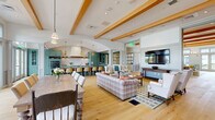 Located at 770 Water Street in Framingham, Massachusetts, this expansive single-floor space offers a thoughtfully designed, open-concept layout encompassing over 2,000 square feet of refined living and gathering areas. Wide-plank light hardwood flooring flows seamlessly throughout, unifying each zone and contributing to the space's warm, welcoming ambiance.

The centerpiece of the space is a chef-caliber kitchen featuring striking teal cabinetry, a large dark-topped island with seating for multiple guests, brass pendant lighting, a statement range hood, and premium stainless steel appliances. Abundant natural light pours in through large windows and glass doors, enhancing the kitchen's vibrant character.

The open lounge and living areas are defined by soaring ceilings with exposed wooden beams and elegant arched architectural details. Multiple seating arrangements — including plaid and upholstered sofas, wingback chairs, and accent tables — create distinct conversation nooks. A wall-mounted flat-screen television serves as a media focal point in one lounge zone.

Additional highlights include a built-in shelving and cabinetry unit in soft blue-gray tones, a classic fireplace, and wainscoting-paneled walls adorned with landscape artwork. Floor-to-ceiling windows in one alcove bathe the space in natural light, while access doors lead to adjacent corridors, completing this elegant and functional communal environment.