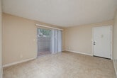 Located at 3950 Waring Rd in Oceanside, CA, this one-bedroom, one-bathroom residence offers a well-organized single-floor layout designed for efficient, comfortable living. The living room features neutral-toned walls, light tile flooring, and a textured ceiling, with a sliding glass door fitted with vertical blinds that opens to a private balcony, allowing natural light to fill the space and providing an outdoor retreat with fenced surroundings. Adjacent to the living room, the combined dining room and kitchen area is outfitted with warm wood cabinetry, a black refrigerator, a built-in dishwasher, and a sink positioned beneath a window. A set of open built-in shelves provides convenient additional storage. The bedroom offers a cozy atmosphere with wall-to-wall carpet, a window with vertical blinds overlooking greenery, and access to a dedicated closet. A hallway connects the main living areas to the full bathroom, which includes a tiled tub-shower combination with chrome fixtures, tile flooring, and a vanity topped with dark granite. The overall palette of warm beige tones and clean finishes creates a cohesive and practical living environment throughout.